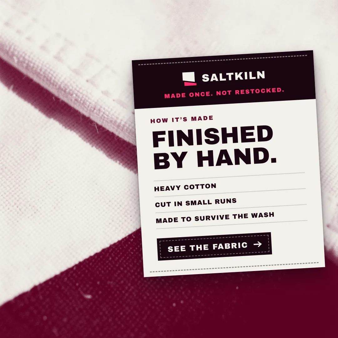A SALTKILN ad with a cream swing tag on white and maroon cotton that reads Finished by hand.
